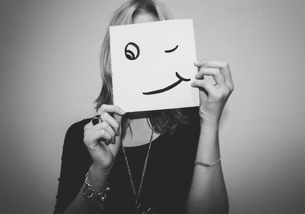 Woman hiding face behind paper with a winking smiley face drawn on it
