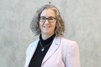 Kiersten Packham smiling, wearing a light suit in an airy, modern room