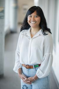 Sarah Mei Lyana smiling, wearing a grey suit in an airy modern room